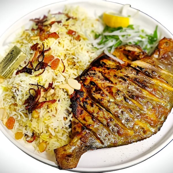Grilled whole fish with rice, nuts, dried fruit, and a lemon wedge on a white plate.
