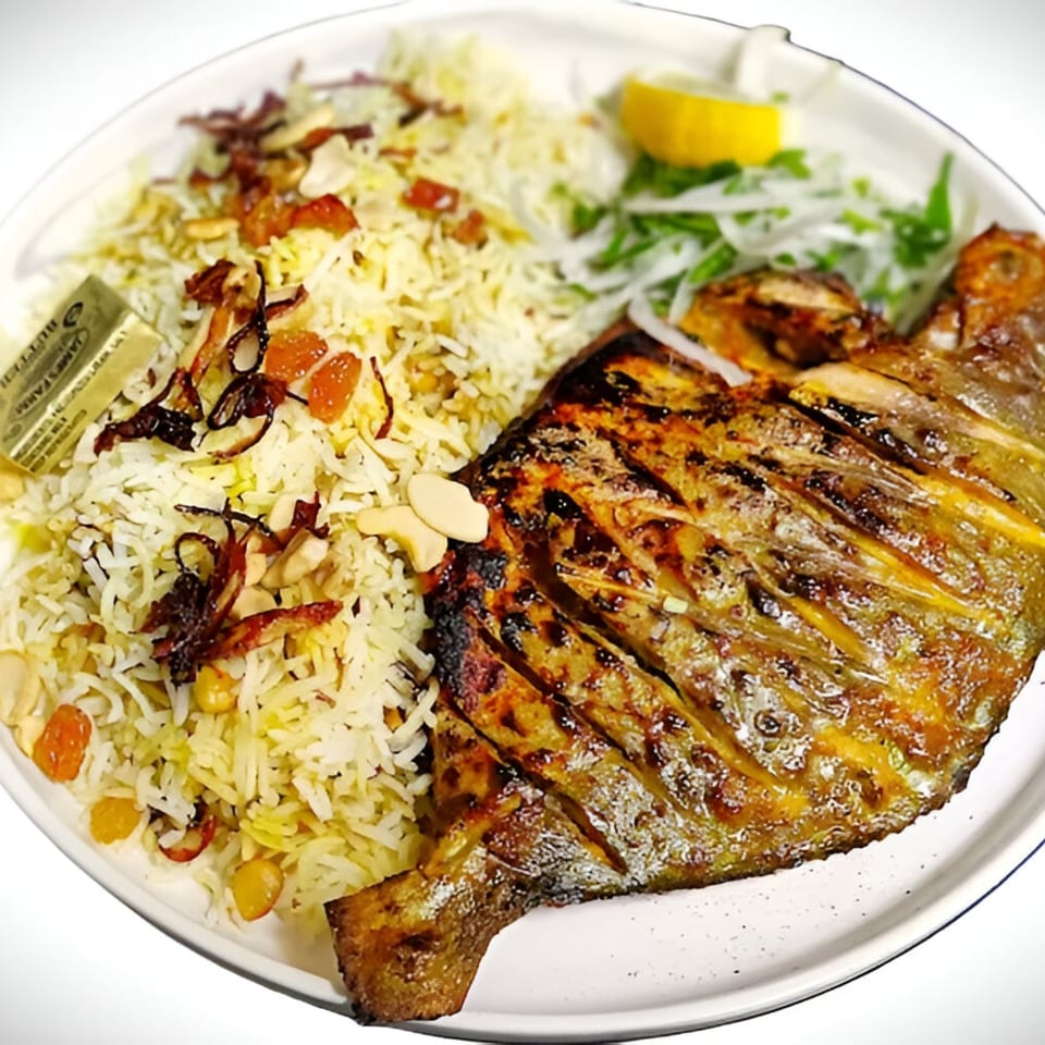 Grilled whole fish with rice, nuts, dried fruit, and a lemon wedge on a white plate.