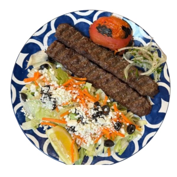 Two Persian kabobs with a grilled tomato, salad, and lemon wedge on a blue and white plate.