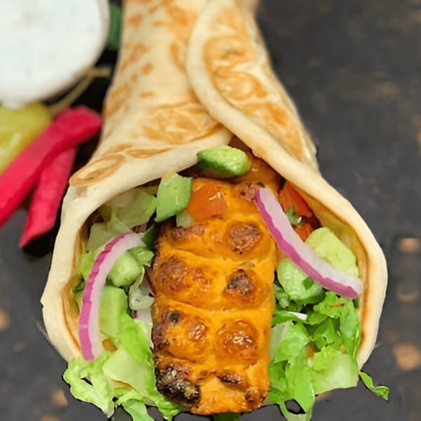 A Persian kabob wrap with grilled chicken, lettuce, red onion, and avocado, served with pickles and sauce.