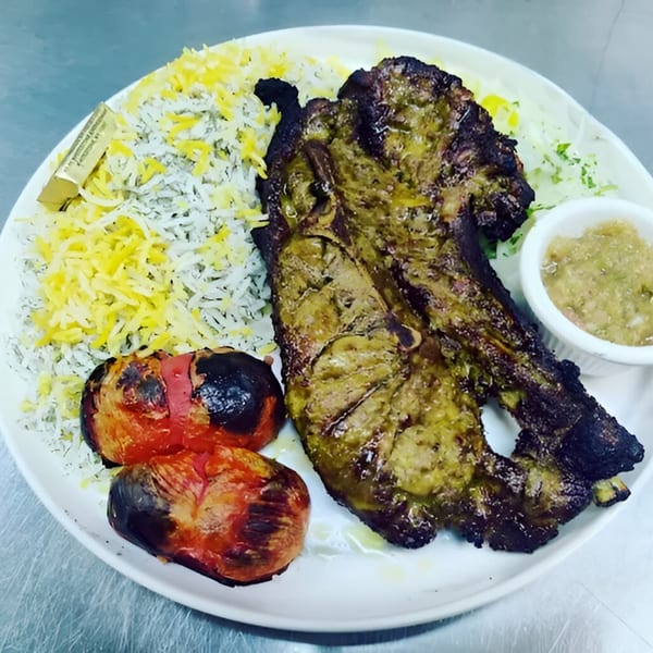 A plate of Persian lamb chops with saffron rice, grilled tomatoes, and a side of sauce.