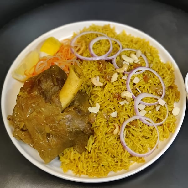 Persian lamb shank with yellow rice, topped with cashews, raisins, and red onion rings.