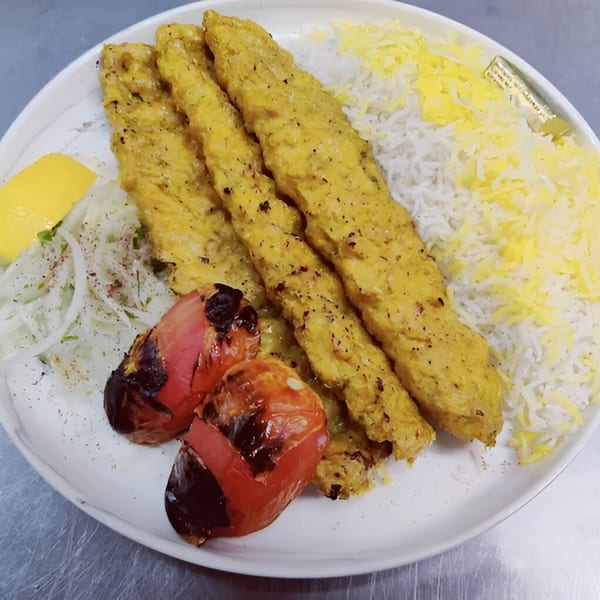 Three chicken kabobs, white rice with saffron, grilled tomatoes, and sliced onions with lemon.
